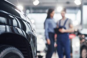 Beautiful young woman is talking to handsome car mechanic while repair a car in dealership